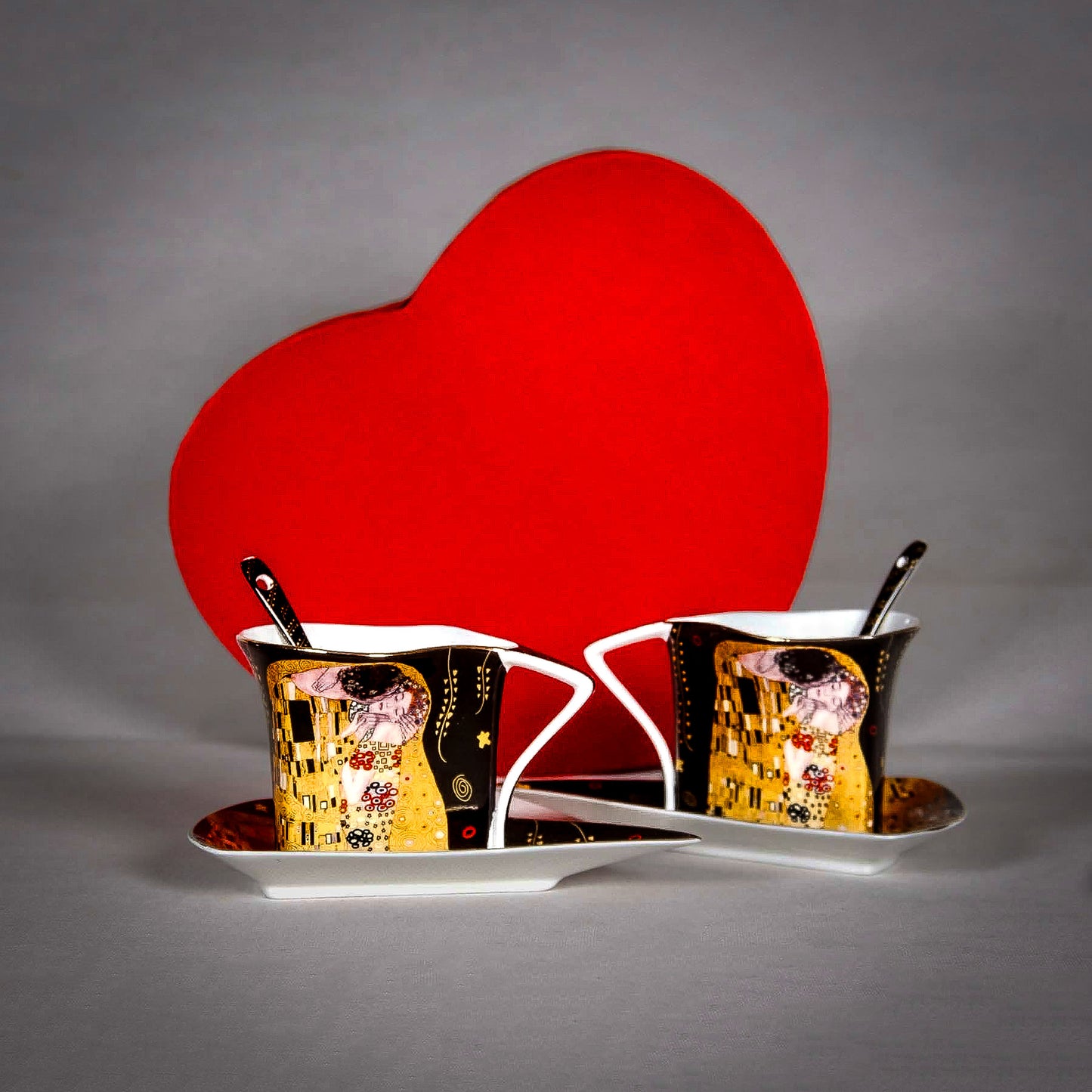 Gustav Klimt "The Kiss" Matching Cups standing on a grey surface, red paper heart behind them